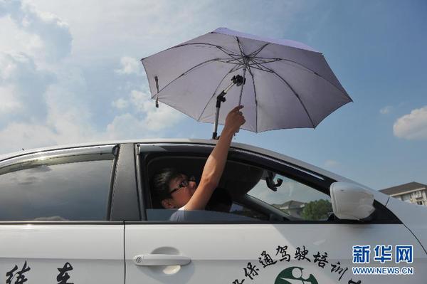 7月20日，在浙江省臨安市一家駕校內(nèi)，一名學(xué)員在車頂架著遮陽傘的教練車內(nèi)練習(xí)。