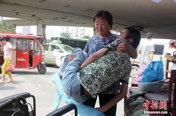 來到街頭“賣唱”點，呂愛梅熟練地把兒子把下三輪車，布置場地。 馬義恒 攝