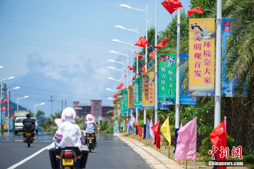 6月24日，海南省文昌市龍樓鎮(zhèn)街道兩側五星紅旗迎風飄揚，火箭“首發(fā)”宣傳廣告隨處可見。長征七號運載火箭發(fā)射日期臨近，中國首個濱海航天發(fā)射中心——文昌航天發(fā)射場所在地海南省文昌市龍樓鎮(zhèn)將迎來“首發(fā)”，中國的“卡納維拉爾角”正揭開神秘面紗。中新社記者 駱云飛 攝